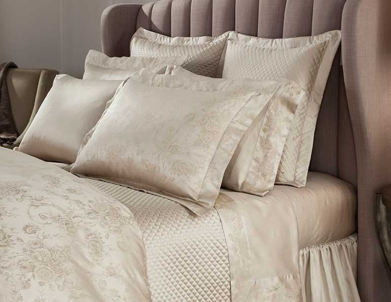 Champagne jacquard floral bedding with quilted accents styled on a bed with layered ivory pillows.