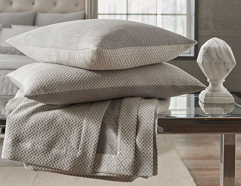 Home Treasures Geneva stacked pillows and folded throw in silver-grey woven texture.