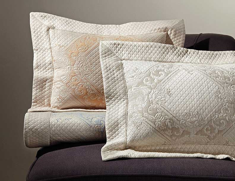 Ivory and champagne quilted pillow shams with ornate medallion embroidery, stacked on dark upholstery.