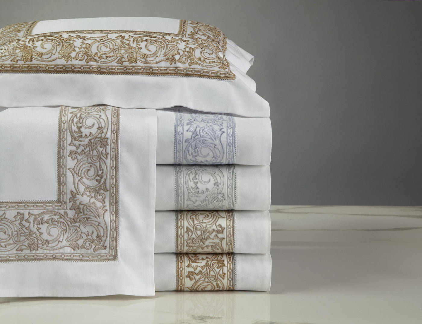 Close-up of folded Home Treasures Paris pillowcases in gold and silver baroque embroidery on white.