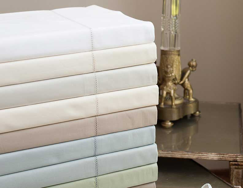 Seven folded Home Treasures Perla yardage pieces stacked, showing ivory, champagne, taupe, and sage colorways.