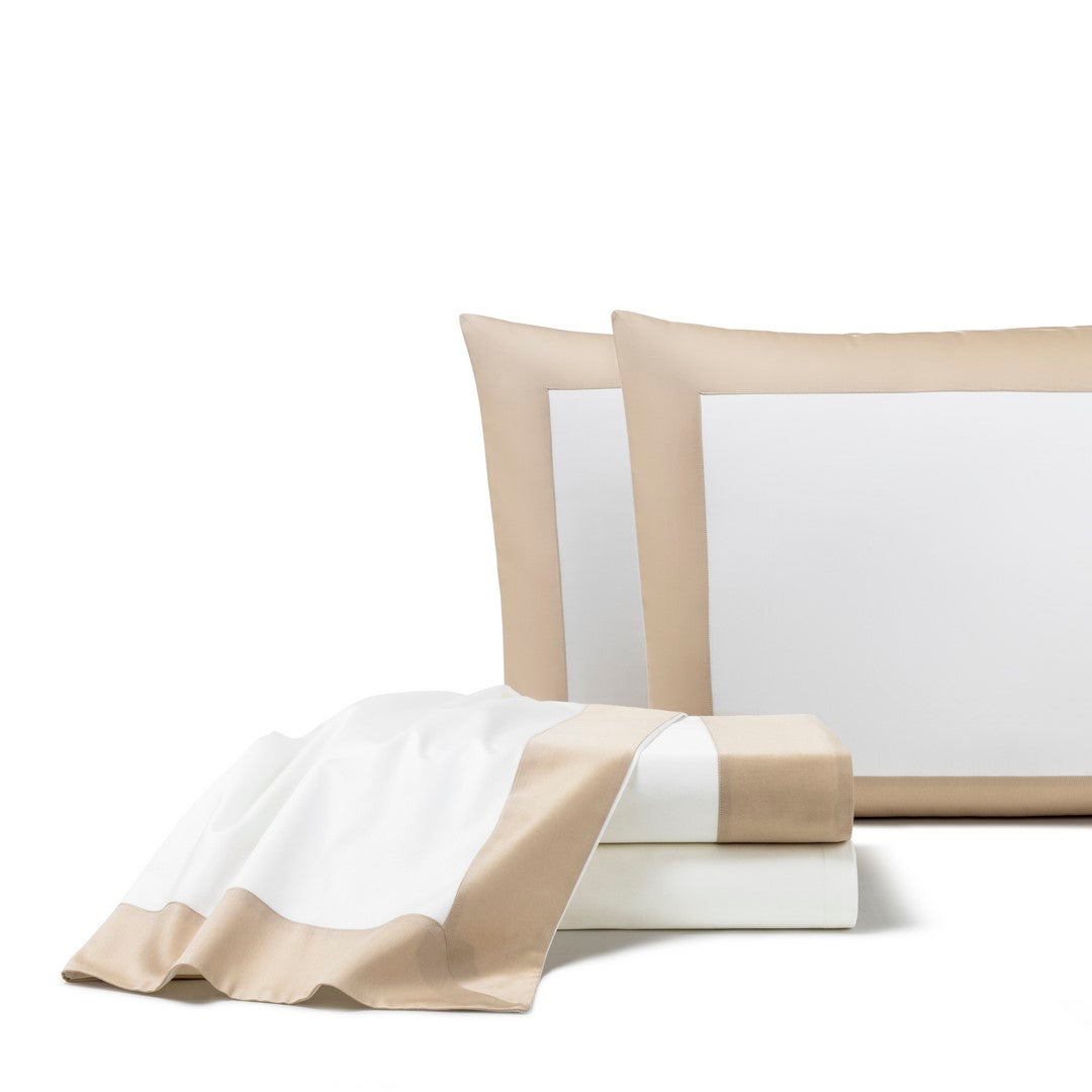 The Bold | Sheet Set by Frette features white bed sheets and pillowcases with beige borders, neatly arranged with a folded blanket in front, offering a modern look to any bedroom.