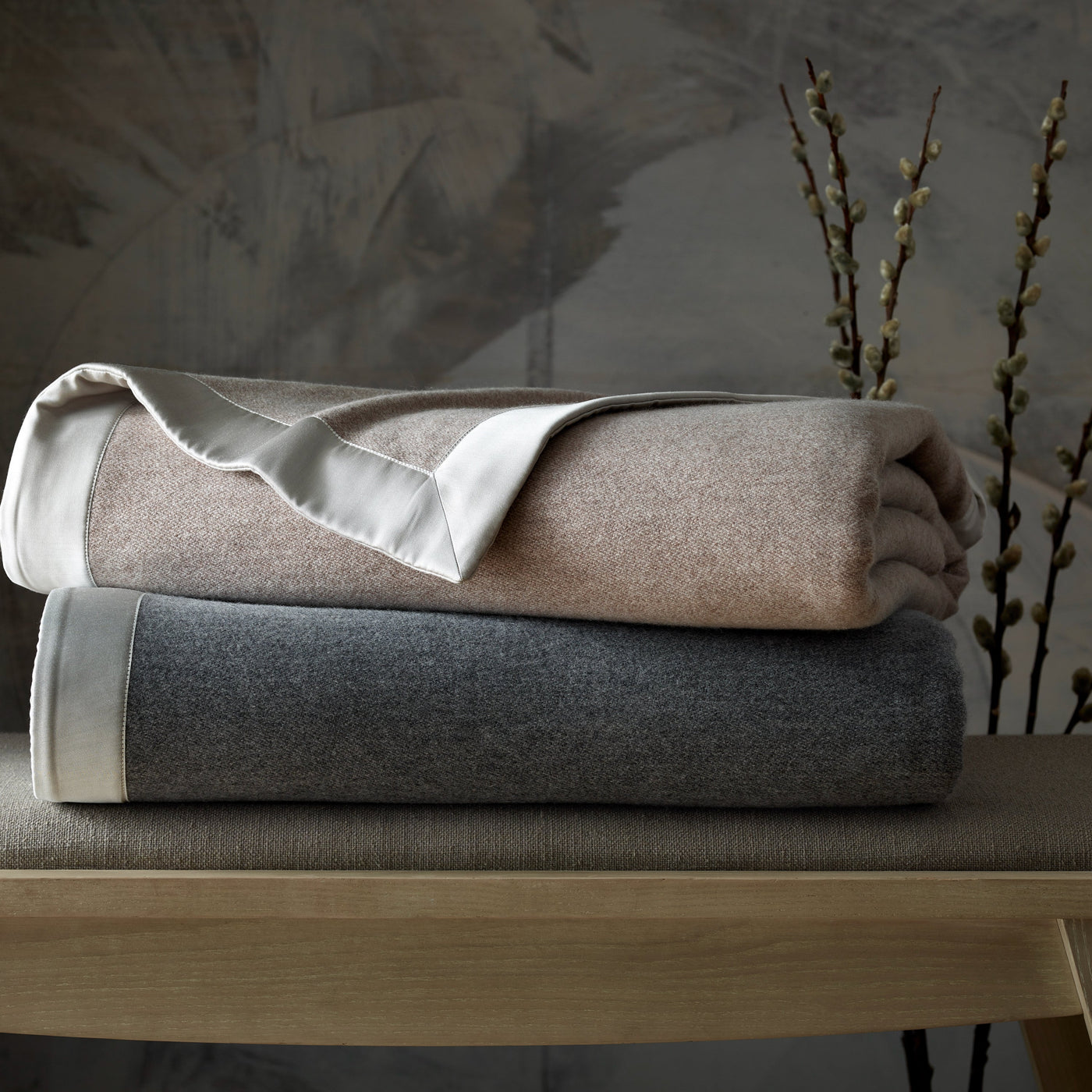 Home Treasures Brunello folded blankets in blush and charcoal with satin trim on bench.