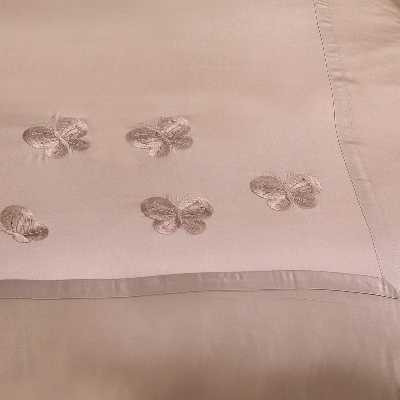 The Kumi Kookoon Butterfly Silk Duvet Cover features light beige silk with embroidered butterfly accents along the border, offering an elegant touch for luxury bedding.