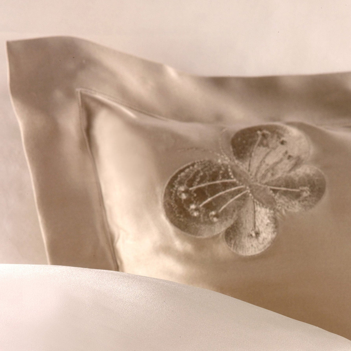 A Kumi Kookoon Butterfly Silk Sham featuring an embroidered butterfly is partially draped by a smooth, white sheet.