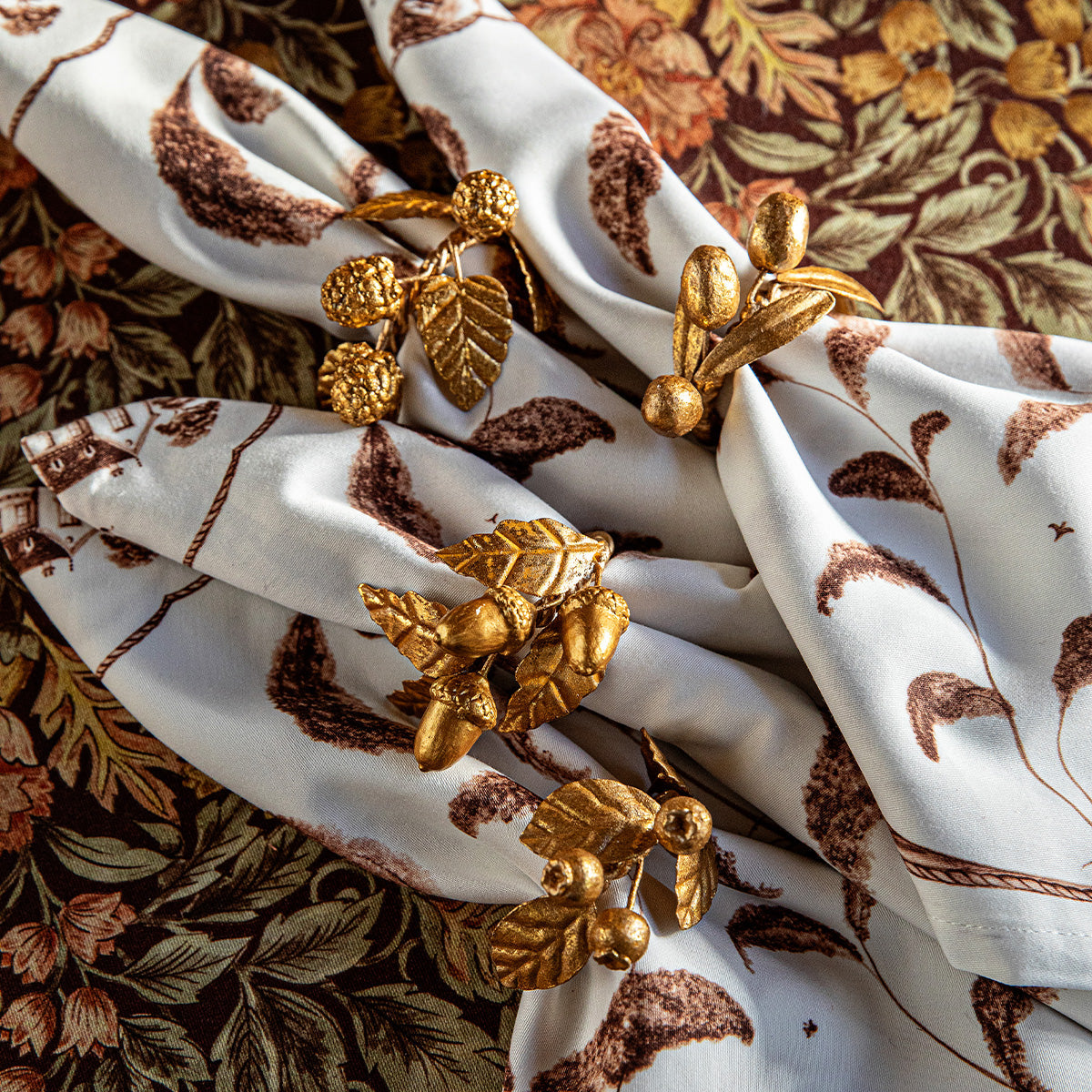 Gold leaf napkin rings on brown and white printed napkins over a floral cloth