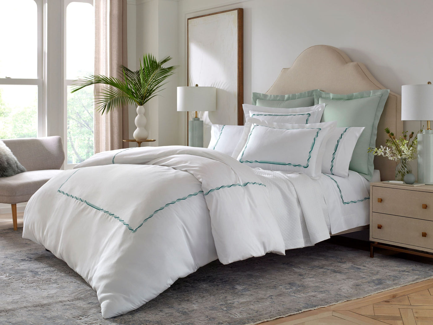 White bedding set with seafoam embroidered trim, styled on a bed in a bright bedroom.