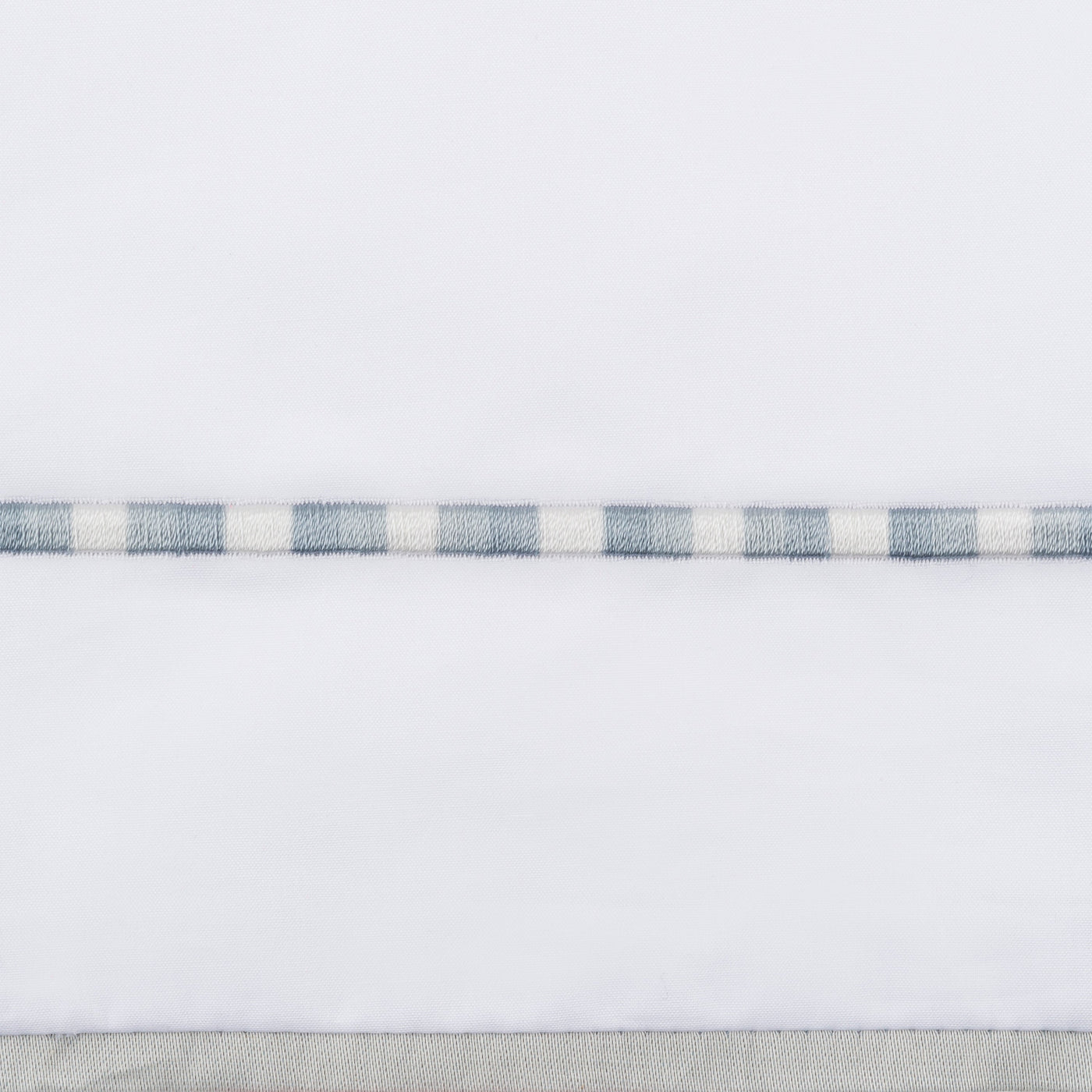 Close-up of slate and ivory checkered embroidered trim on white flat sheet hem.