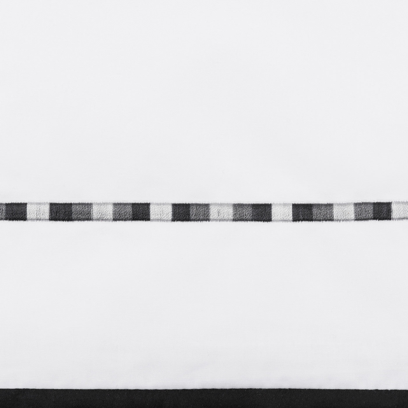 Close-up of black and white woven checkerboard border trim on white cotton flat sheet.