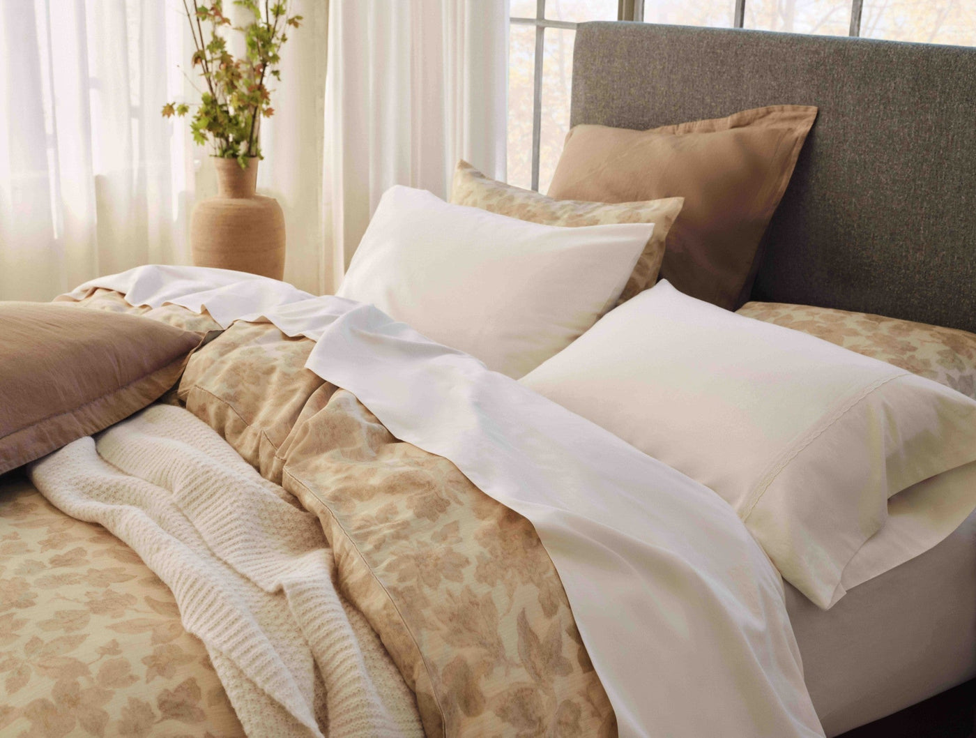Camellia Print duvet cover in warm camel tones styled on a bed with white pillows and sheer curtains.