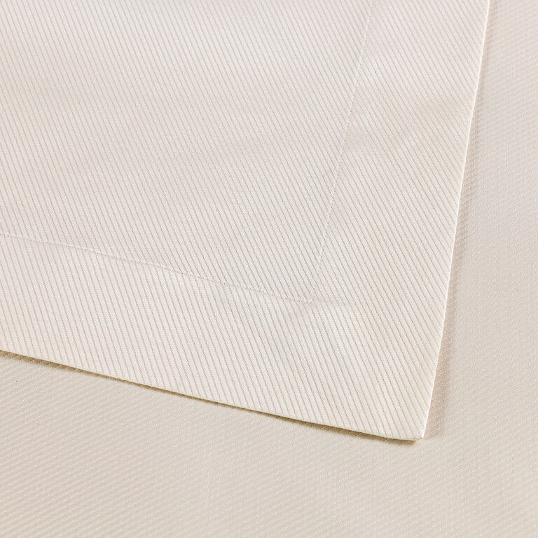 Close-up of Frette's Cavalry bedspread, crafted from cream-colored, diagonally striped cotton jacquard with a mitered corner, neatly folded on a matching background.