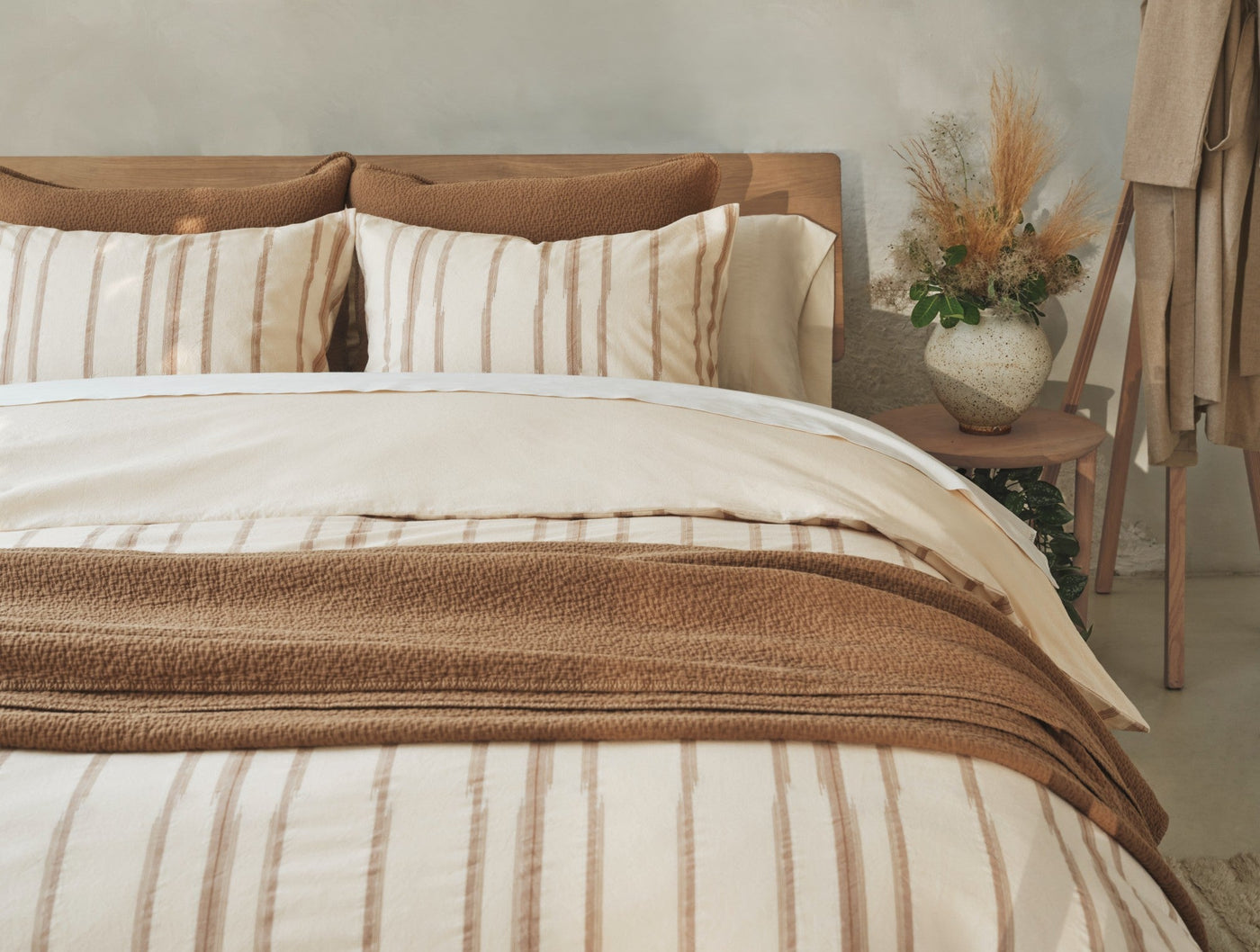 Coyuchi Cazadero Stripe duvet cover styled on bed with camel throw blanket and dried floral arrangement.
