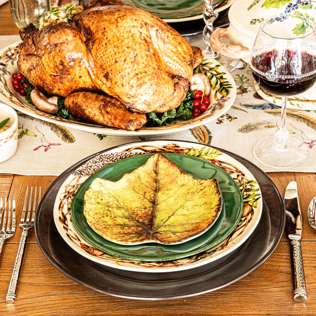 Green Forest Walk leaf plate on a place setting with a roast turkey and red wine behind