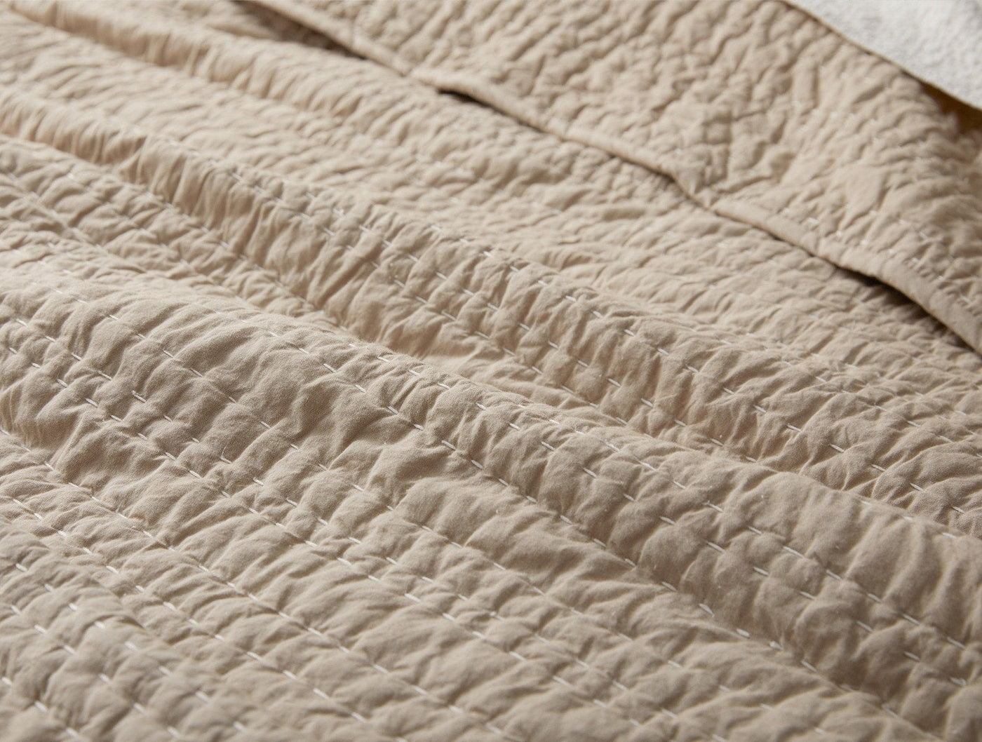 Close-up of Coyuchi Channel Handstitched quilt showing sand-toned rippled stitching texture.
