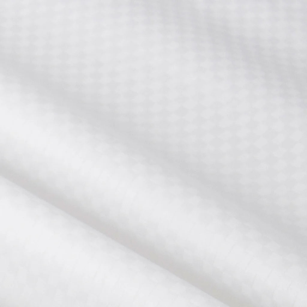 Close-up of Frette’s Checkered Sateen Pillow Sham Set, featuring a white sateen fabric with a subtle diamond checkered pattern and soft folds, evoking the luxurious feel of boutique hotel bedding.