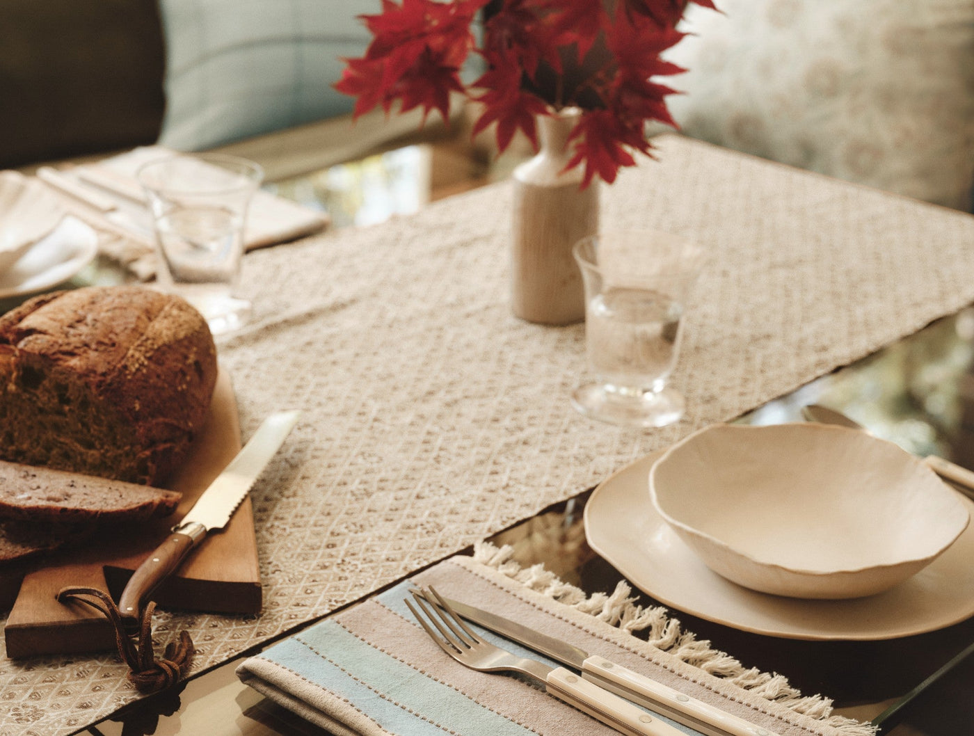 Ivory Coyuchi Coral Bell table runner styled with placemats, dinnerware, and red floral centerpiece.