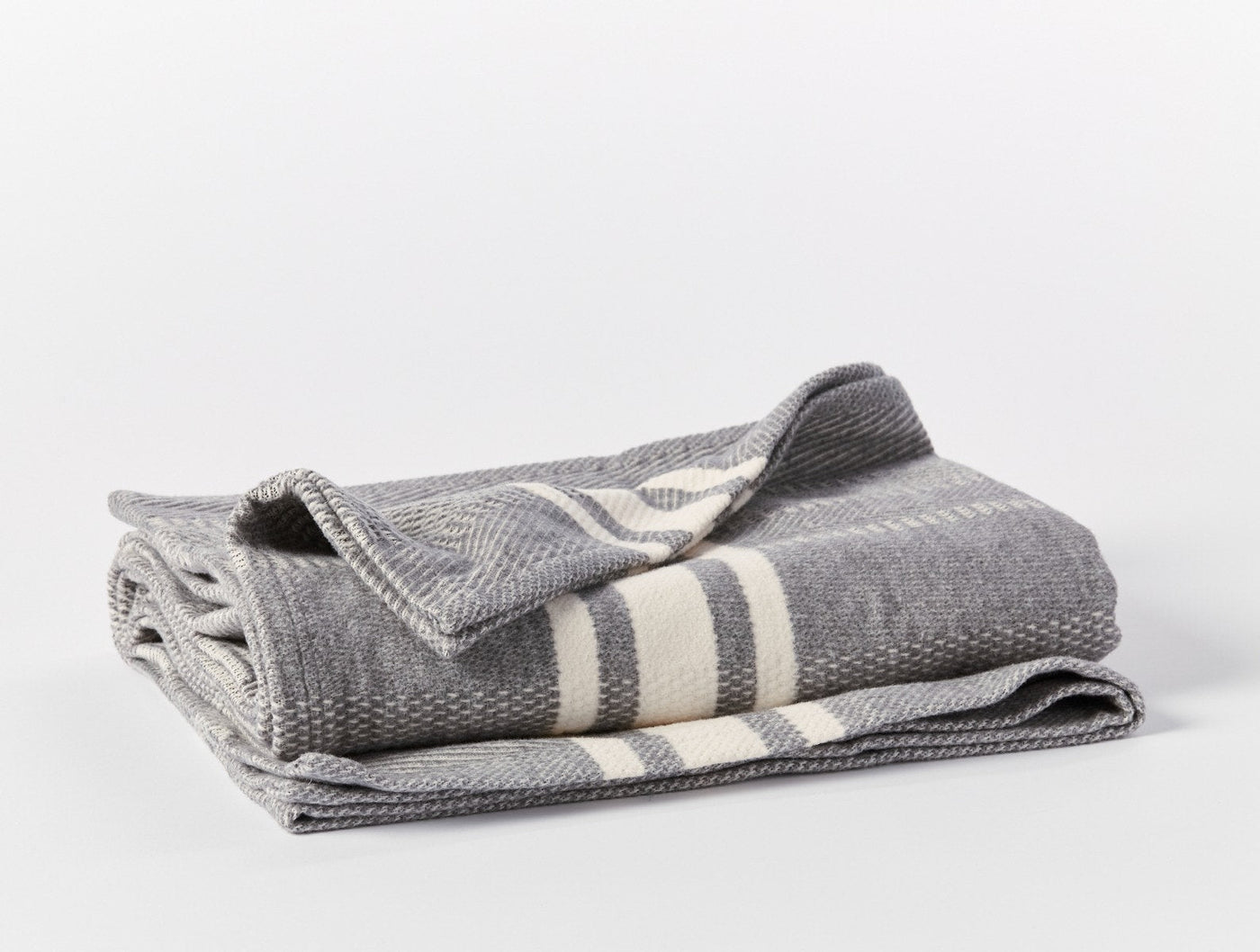 Ivory stripe detail on folded grey Coyuchi Cirrus Supersoft throw, herringbone weave visible.