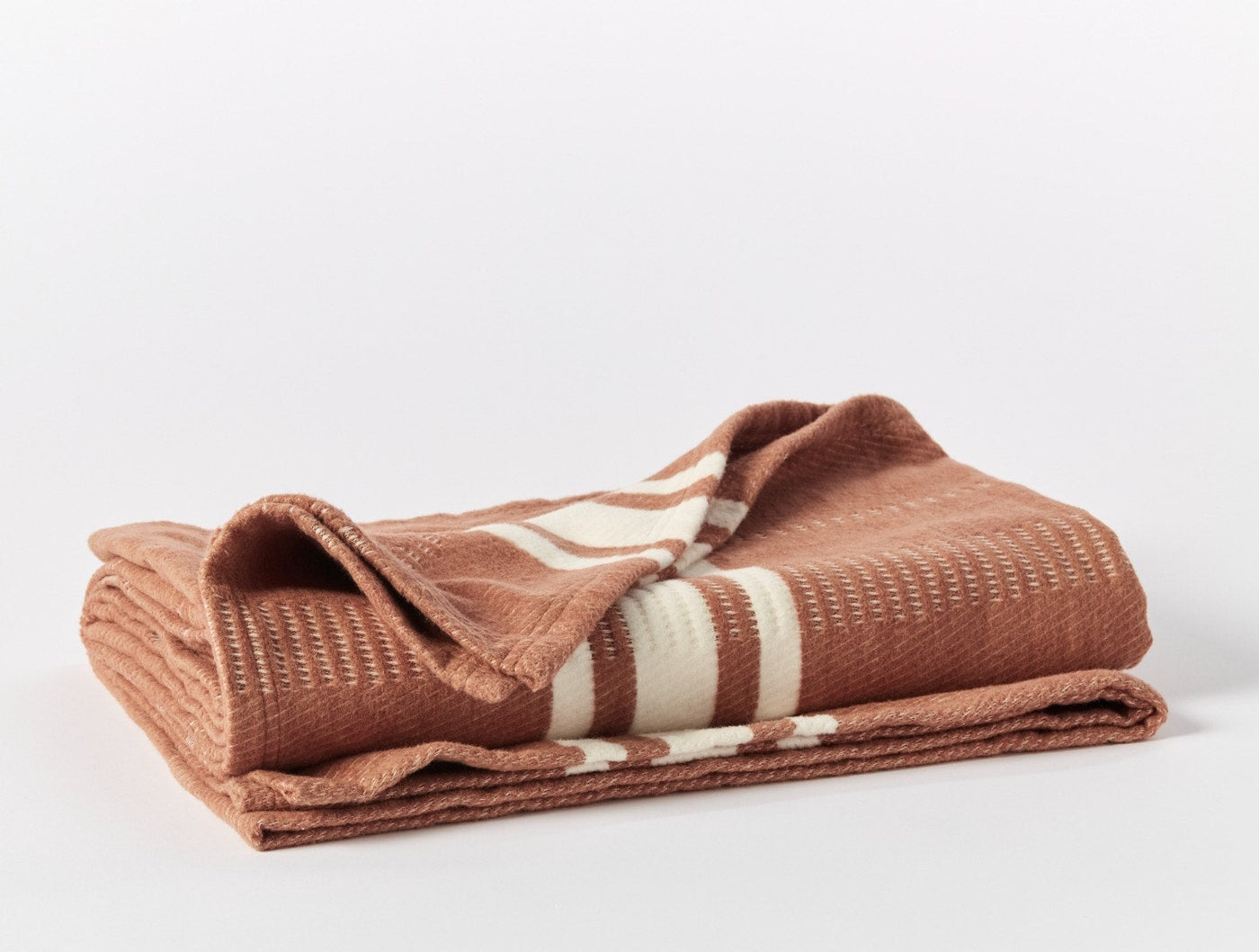 Close-up of folded terracotta Coyuchi Cirrus Supersoft throw showing ivory stripe detail and waffle texture.