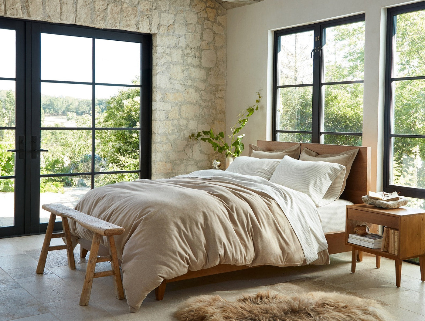 Ivory flannel pillow shams styled on a made bed in a sunlit stone-wall bedroom.