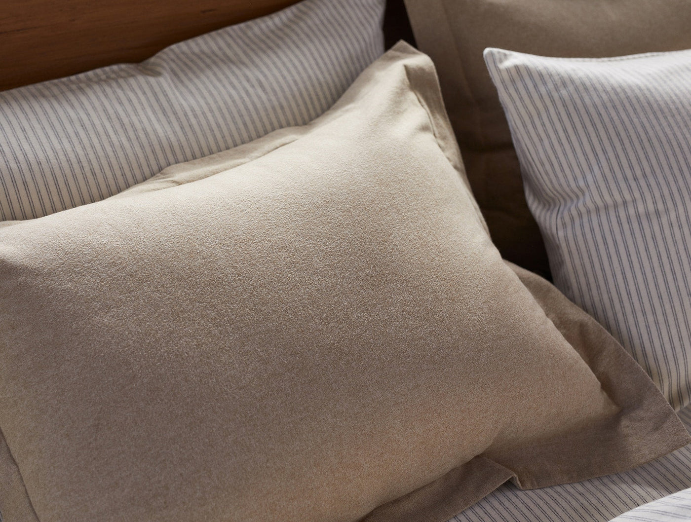 Close-up of a sand brushed flannel pillow sham layered with striped shams on a bed.