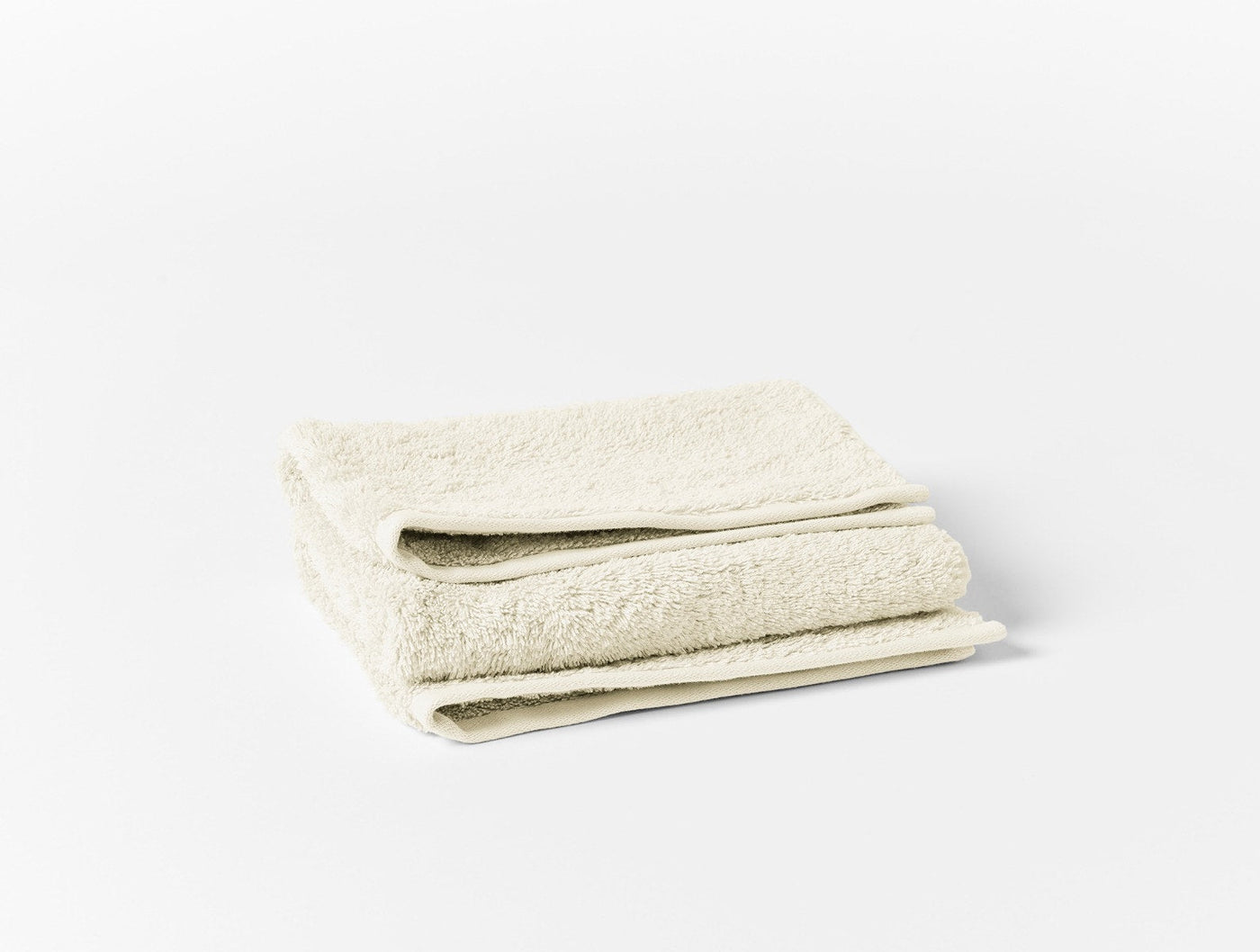 Folded ivory organic cotton terry hand towel showing plush loop texture and hem detail.