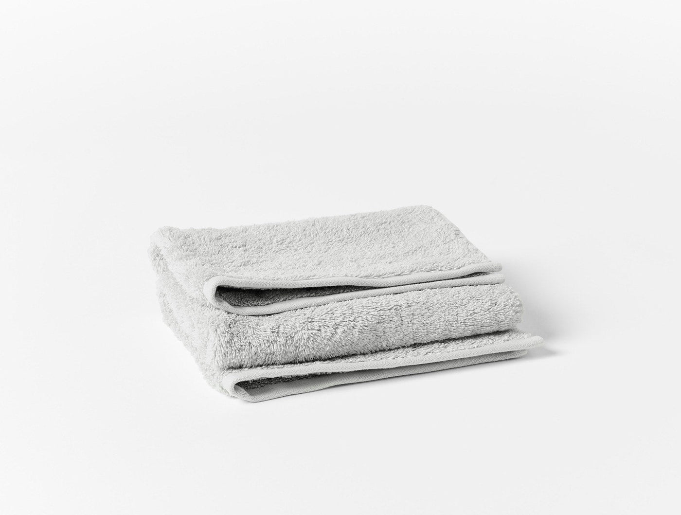 Folded silver grey terry bath sheet showing plush looped texture, stacked on white surface.