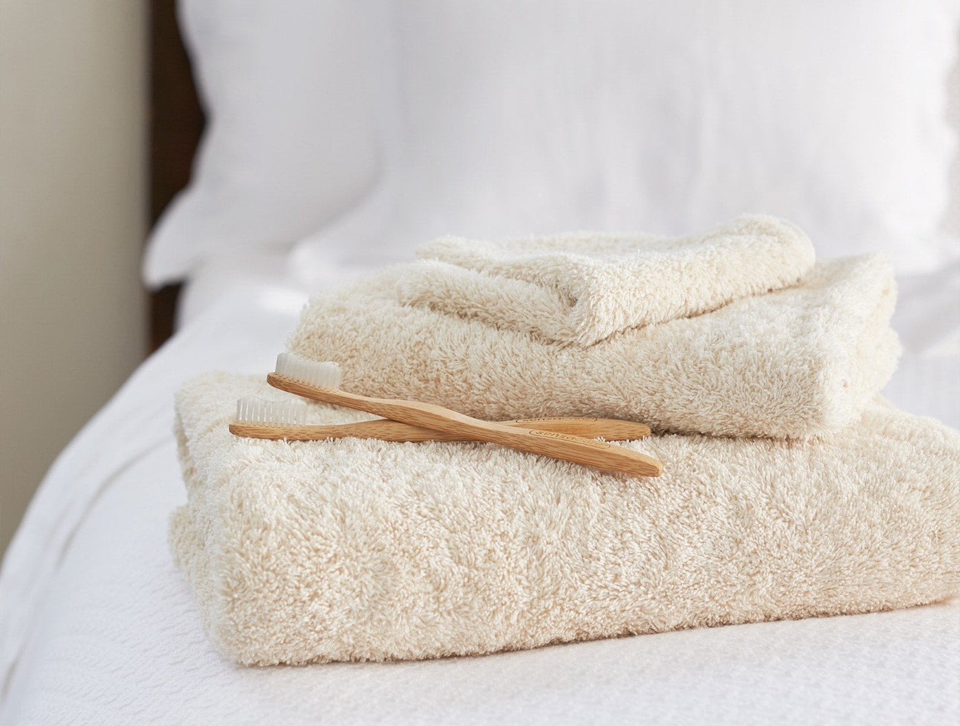 Coyuchi Cloud Loom hand towels stacked in ivory with bamboo accessories on white bedding.