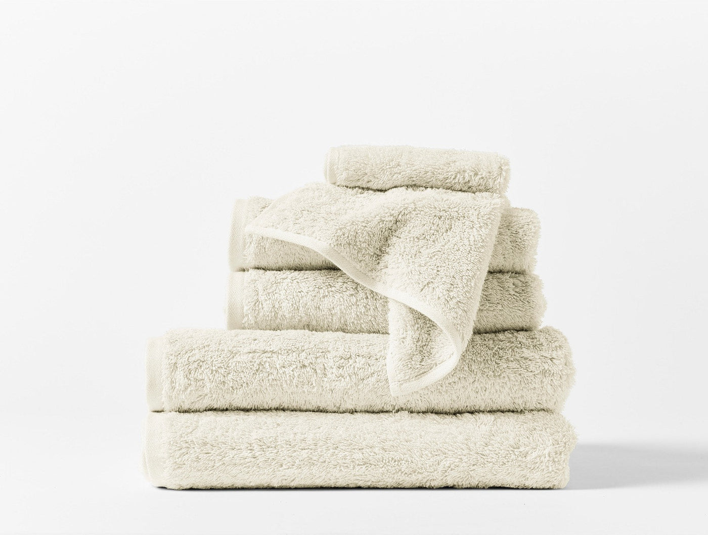 Stacked ivory Coyuchi Cloud Loom towels in assorted sizes against white background.