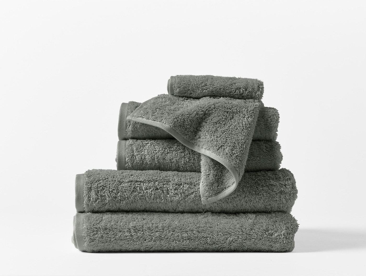 Close-up of stacked sage Coyuchi Cloud Loom towels showing plush looped texture and folded hem.