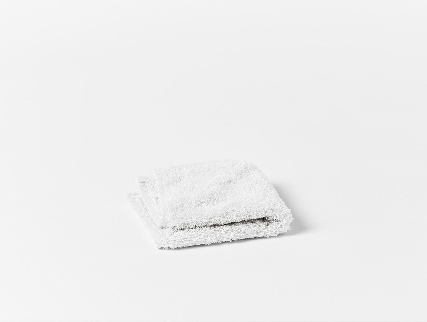 Folded white terry hand towel shown from above on a white surface.