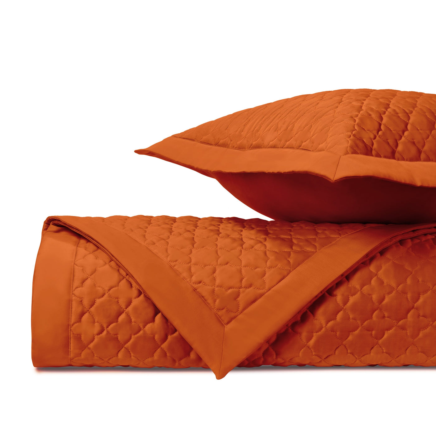 Close-up of clover diamond quilting pattern in burnt orange on folded coverlet and sham.