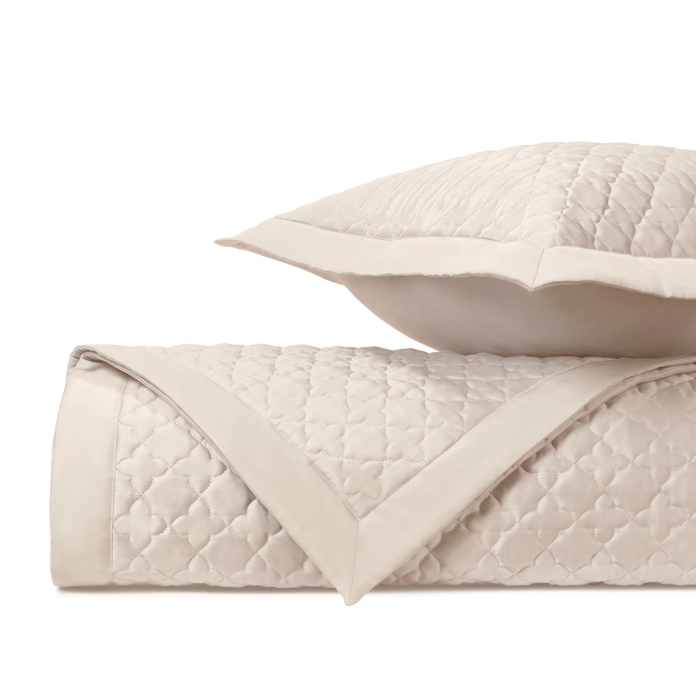 Close-up of ivory quilted diamond-pattern coverlet and sham with satin border trim.