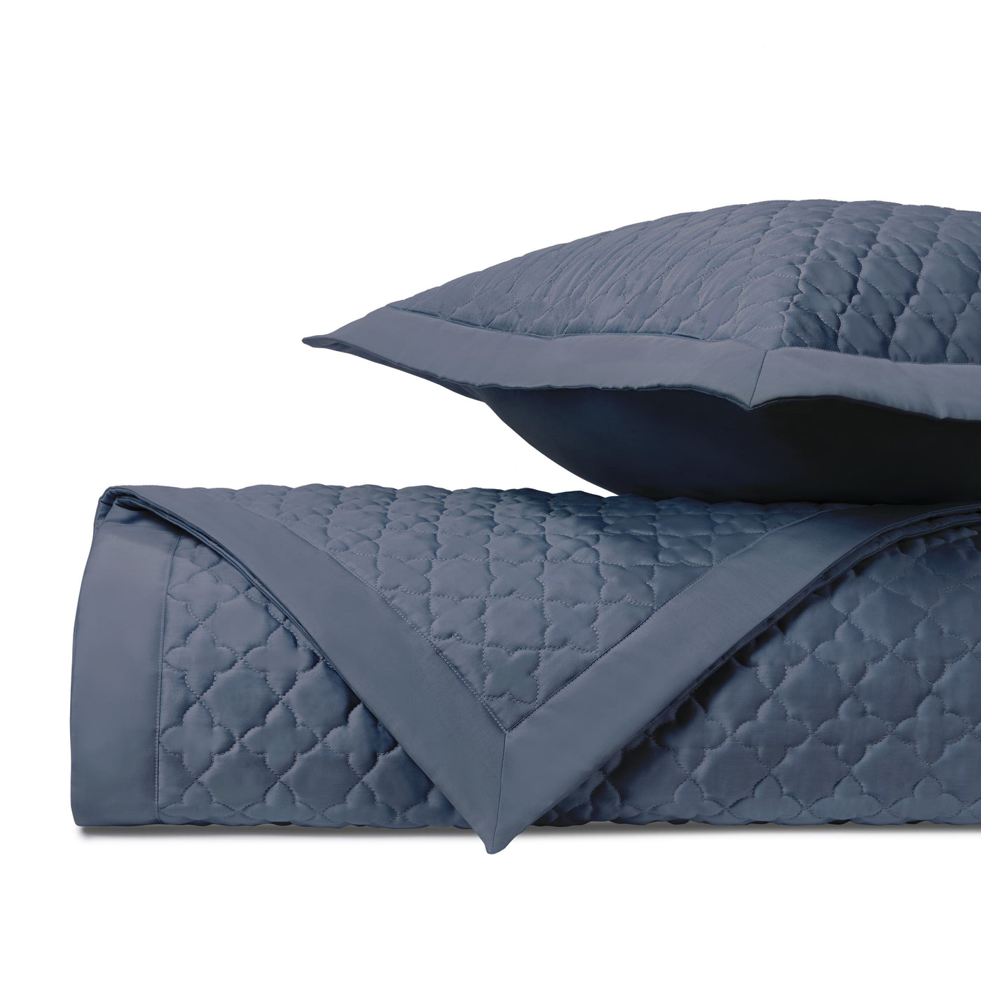 Close-up of navy blue quilted clover-pattern coverlet and sham with contrast border trim.
