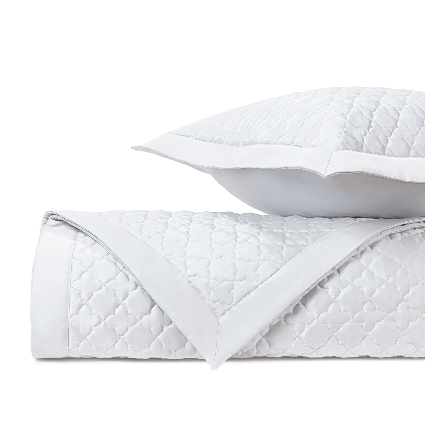 White quilted cotton clover-pattern coverlet rolled with matching sham, white border detail.