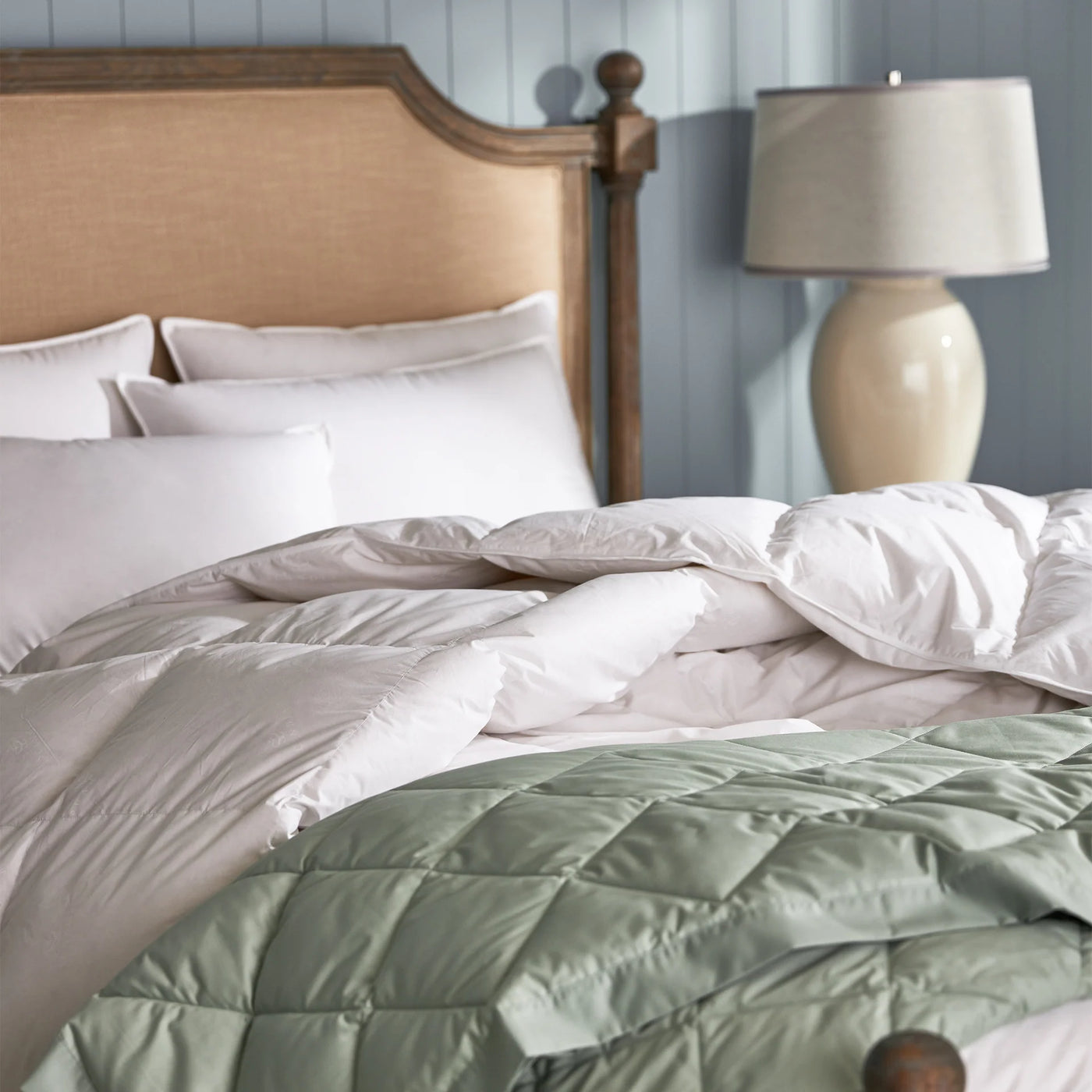 White duvet with sage quilted blanket layered at foot of bed, angled lifestyle view.