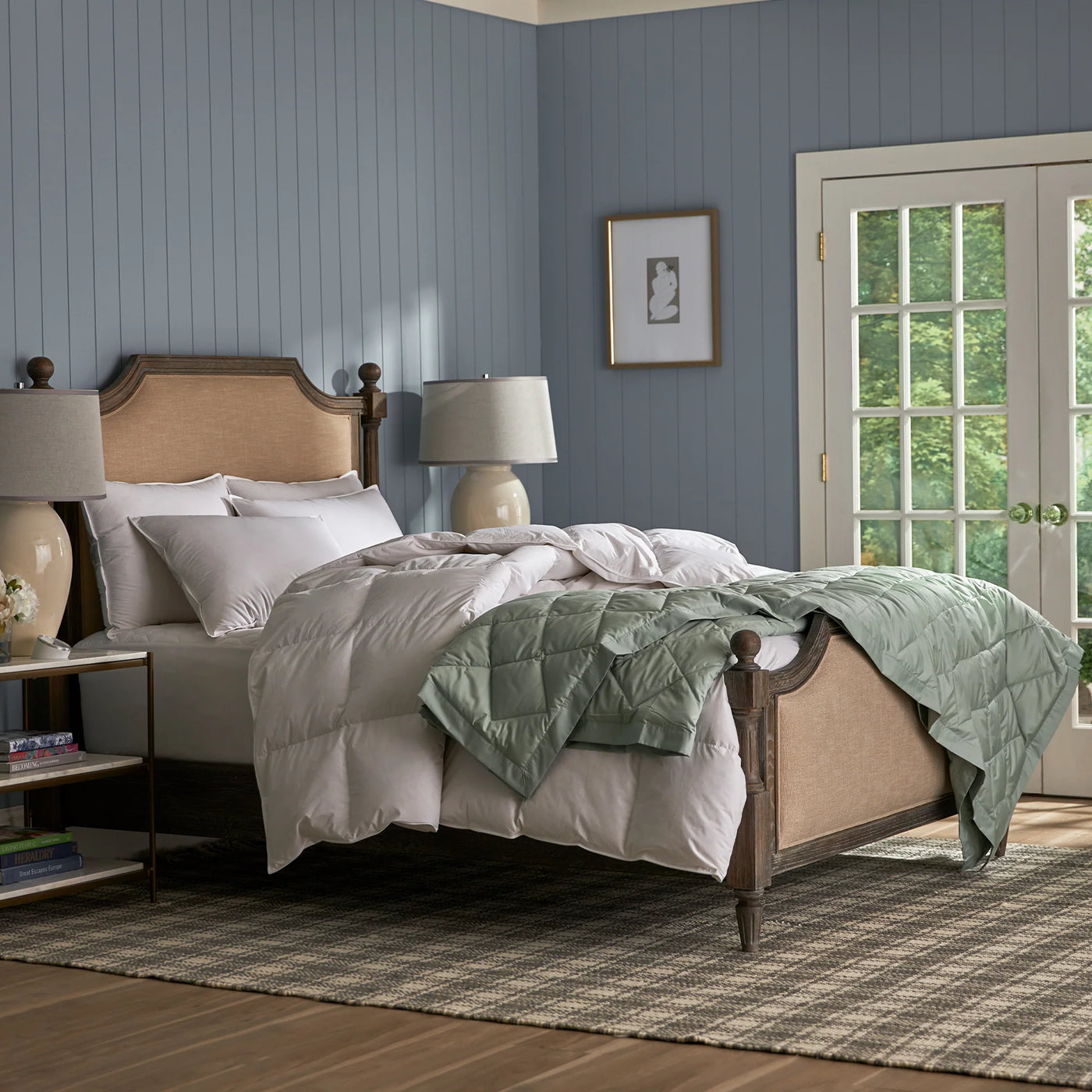 Sage green quilted blanket draped over white bedding on a wood and cane bed.