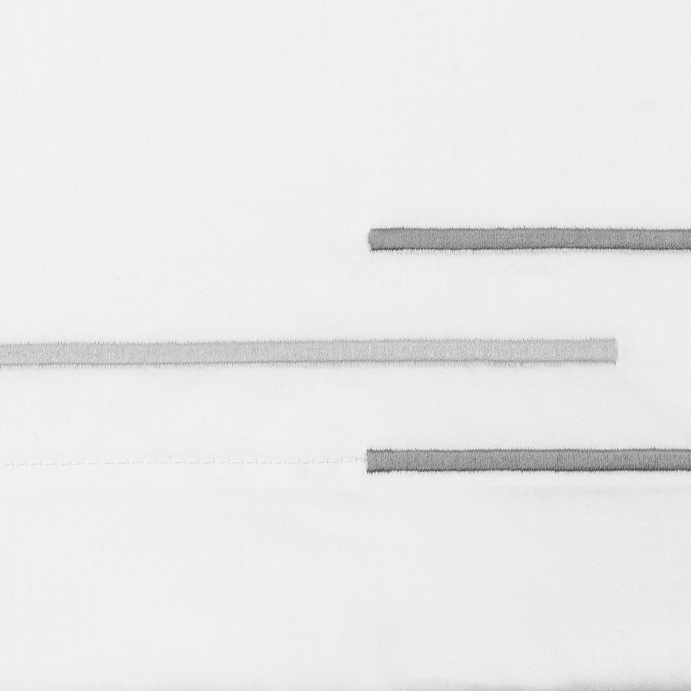 Close-up of staggered silver satin-stitch embroidery lines on white cotton fabric.