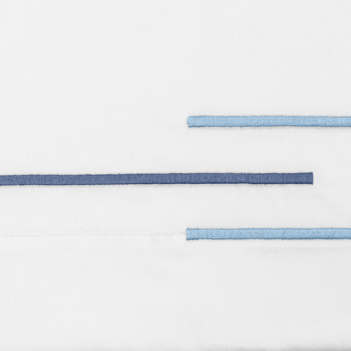 Close-up of Corso satin stitch embroidery in navy and sky blue on white cotton.