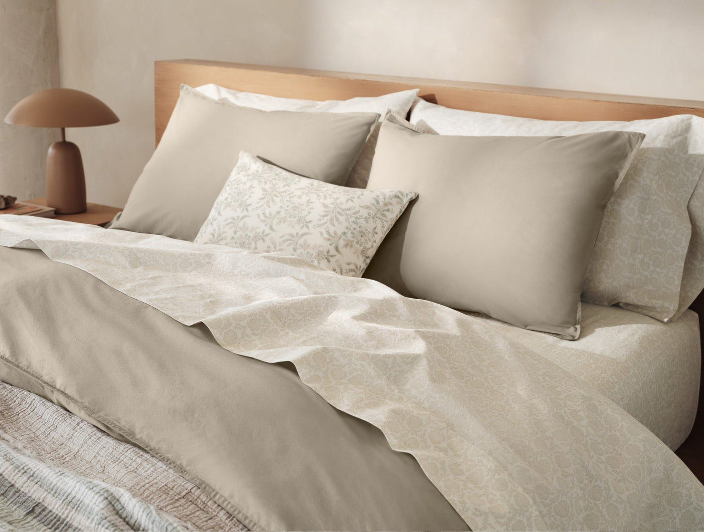 Taupe crinkled percale pillow shams styled on a made bed with layered neutral bedding.