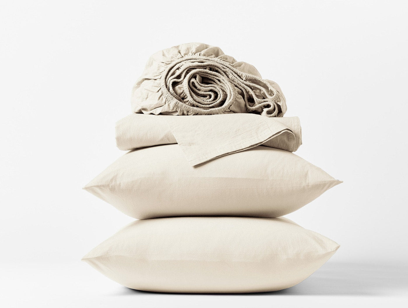 Rolled and folded ivory crinkled percale sheets stacked atop two pillowcases on white background.