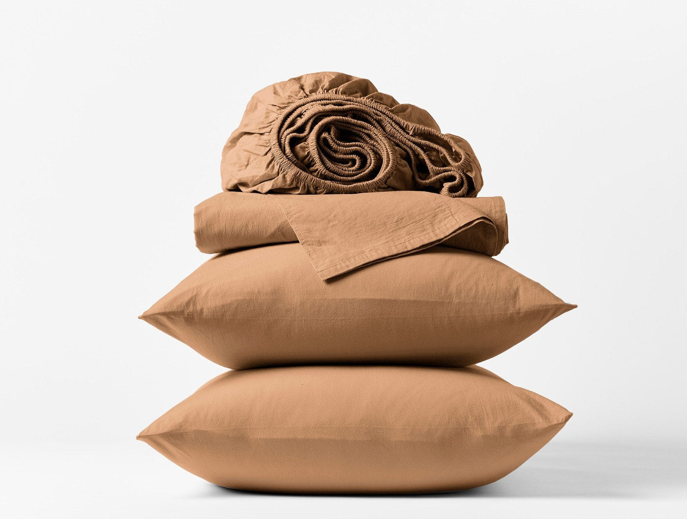 Close-up of stacked caramel Coyuchi Crinkled Percale pillowcases and folded sheets on white background.