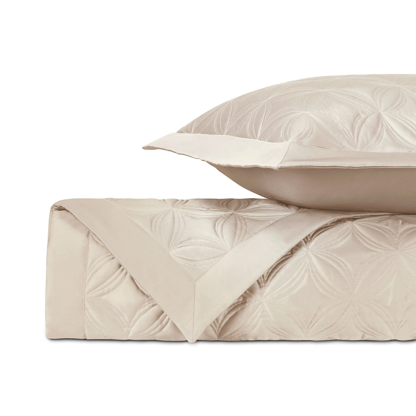 Close-up of ivory quilted coverlet with floral geometric pattern, folded with matching sham.