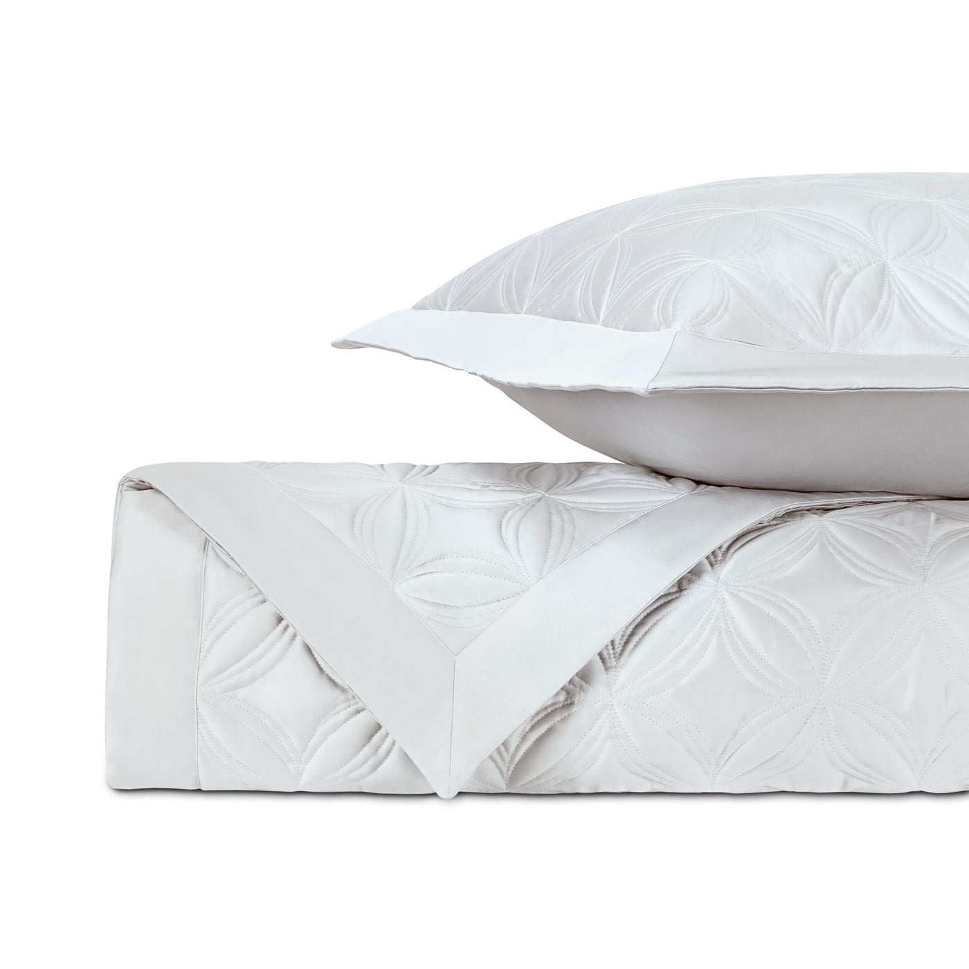 Close-up of white quilted coverlet with embossed floral medallion pattern, folded with matching euro sham.