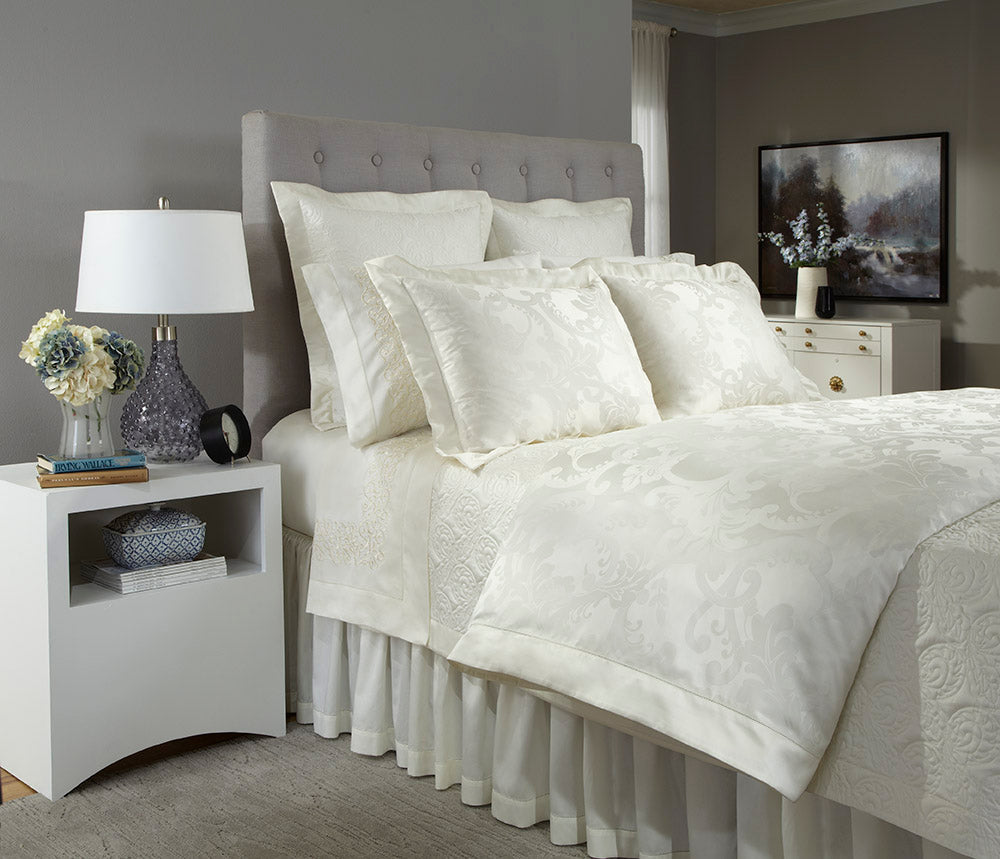 Close-up of ivory damask fabric texture on a fully styled bed.
