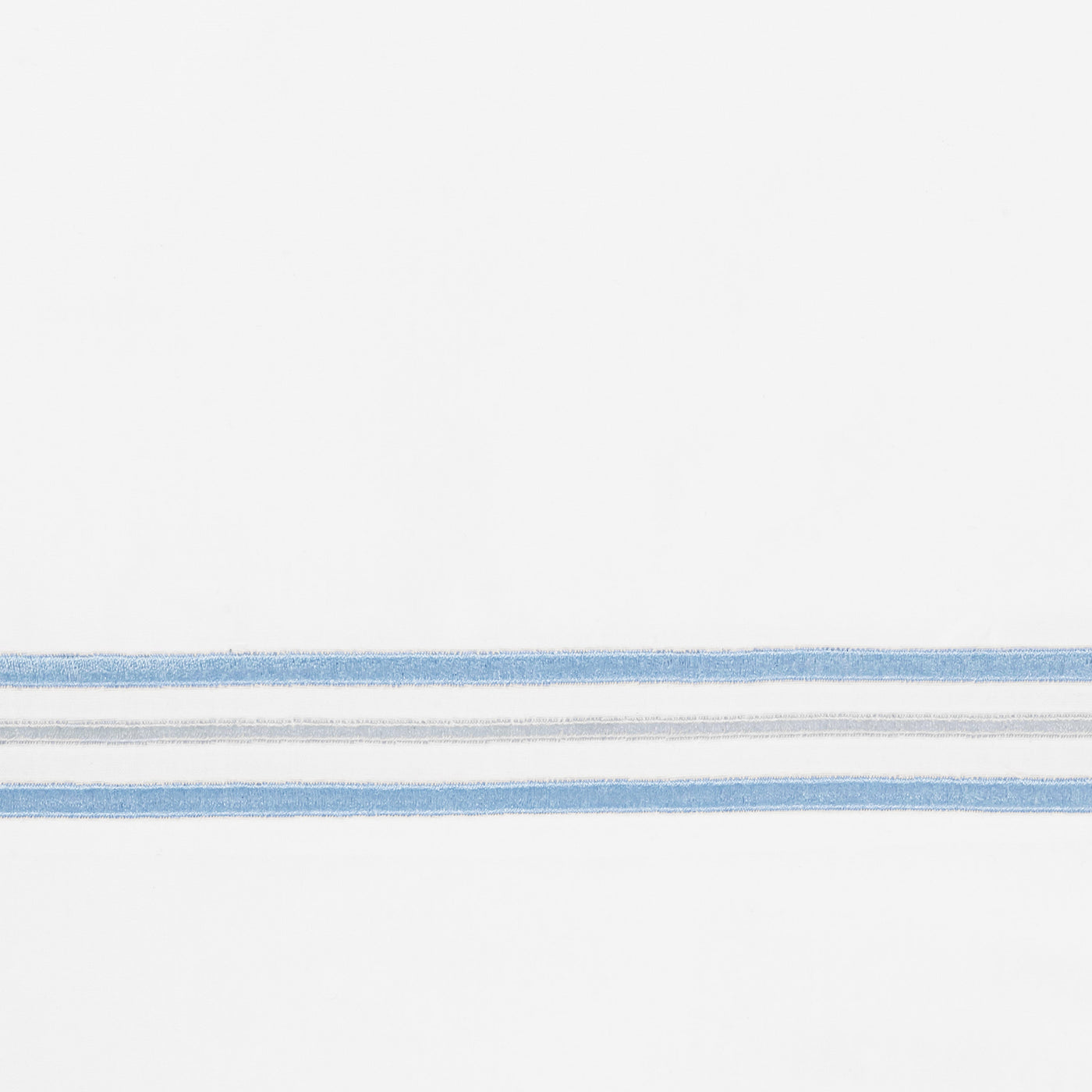 Close-up of blue and silver embroidered stripe border on white cotton fabric.