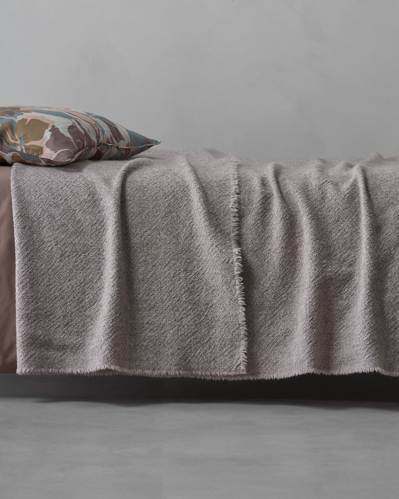Society Limonta Des blanket in mauve draped over bed edge, showing fringe detail.