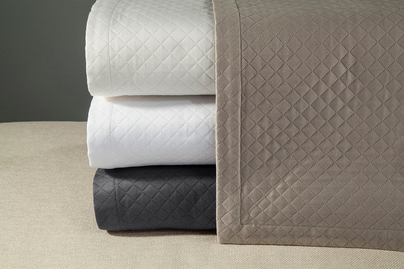 Close-up of folded Diamante quilts in ivory, white, charcoal, and taupe colorways.