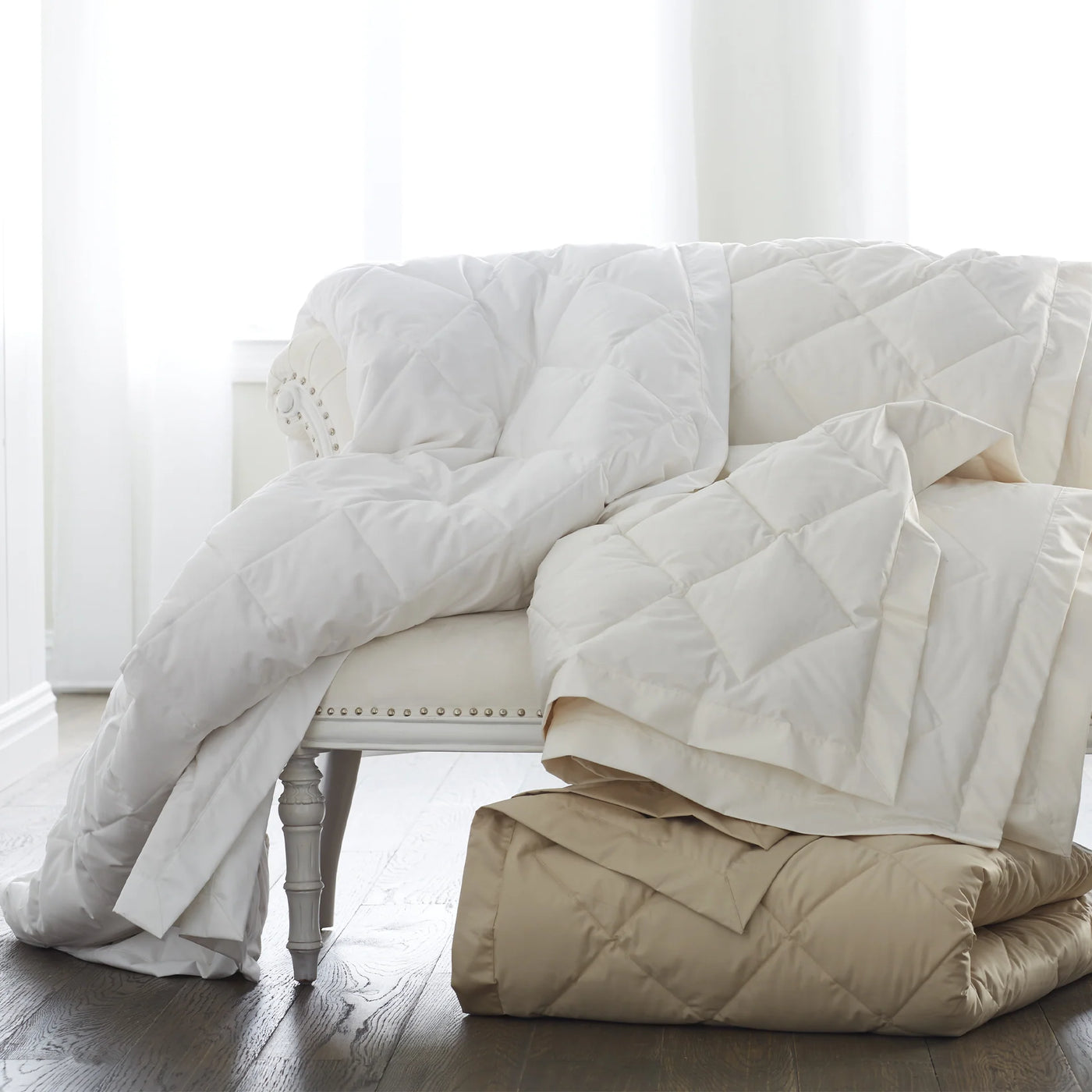 Scandia Home Down Blanket in white draped over chair with champagne folded blanket on floor.