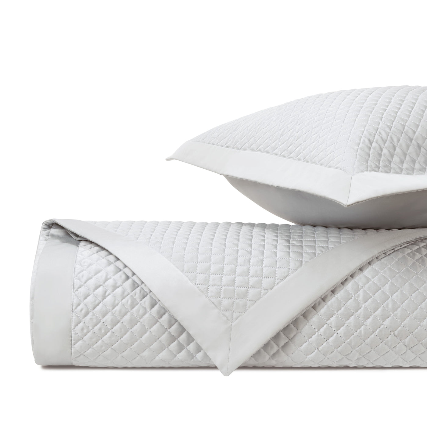 Close-up of white diamond-quilted texture with sateen border on folded coverlet and sham.