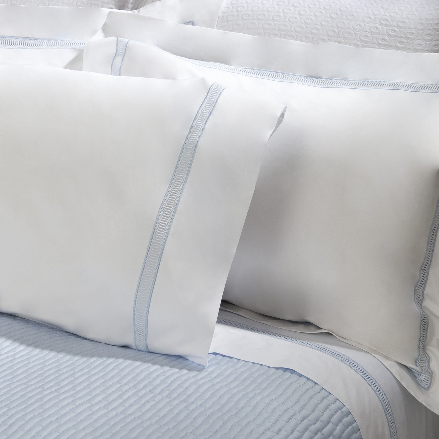 Close-up of white cotton pillowcase with pale blue embroidered border detail.
